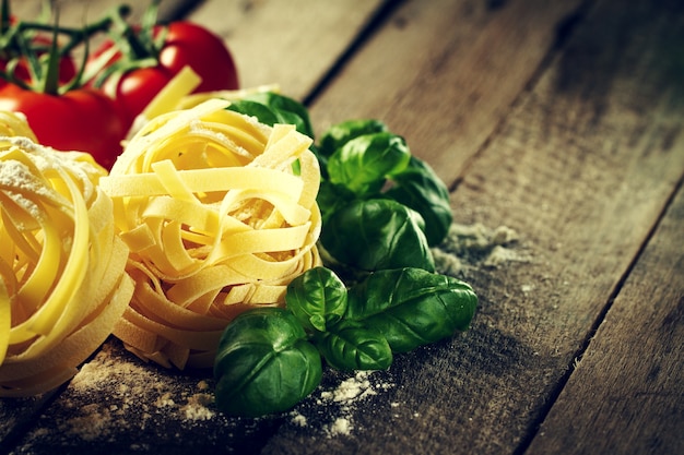 Ingredientes coloridos frescos saborosos para cozinhar tagliatelle da massa com manjericão fresco e tomates. fundo de madeira da tabela.