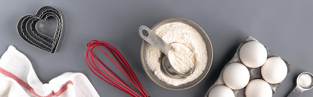 Foto grátis ingredientes para assar em um fundo cinza escuro: farinha, ovos, fermento em pó, forma de coração, batedor, têxteis. vista do topo. layout de uma receita de torta ou bolo com biscoitos. bandeira