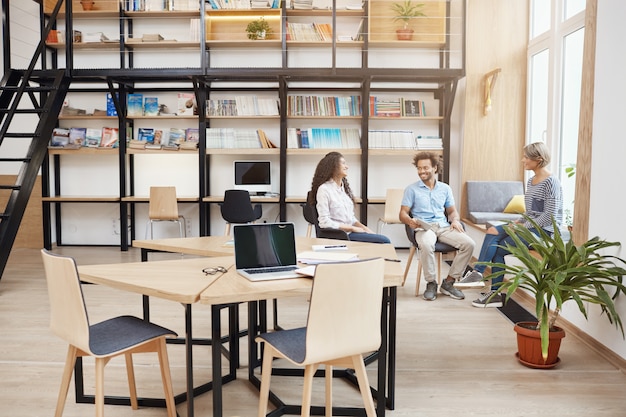 Inicialização, negócios, conceito de trabalho em equipe. Grupo de jovens de perspectiva em reunião na grande biblioteca moderna falando sobre os lucros do último projeto, olhando os papéis, sorrindo e tendo tim produtivo