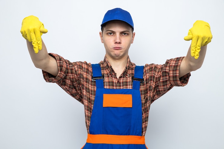 Foto grátis insatisfeito, fingindo estar segurando algo, jovem faxineiro de uniforme e boné com luvas