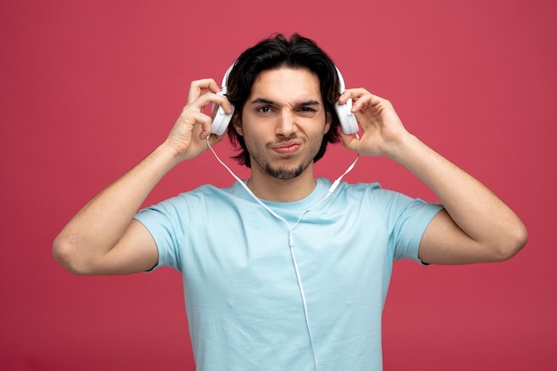 insatisfeito jovem bonito olhando para a câmera tirando os fones de ouvido isolados no fundo vermelho