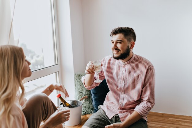 Instantâneo de casal apaixonado, desfrutando de champanhe. Homem com barba olha suavemente para a namorada.