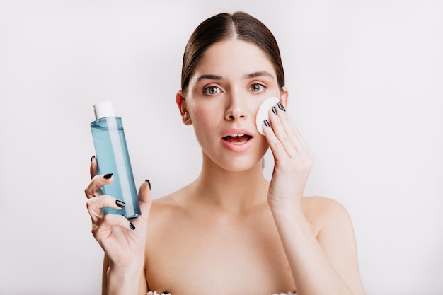 Instantâneo de menina bonita sem maquiagem limpando o rosto de impurezas usando água micelar