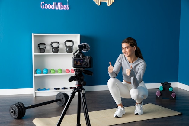 Foto grátis instrutor de fitness feminino ensinando uma aula on-line em casa usando uma câmera no tripé