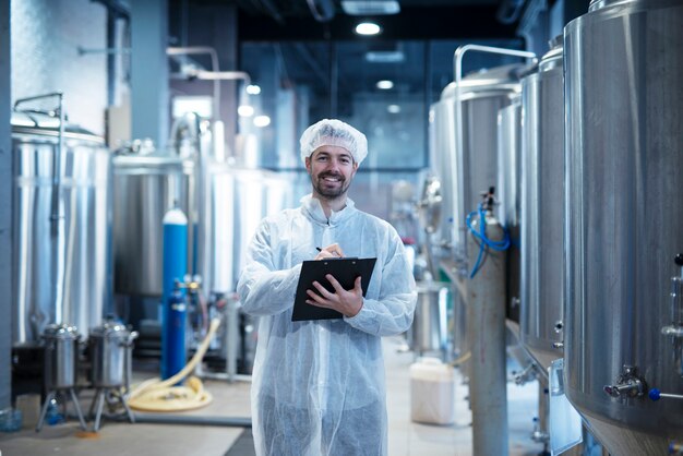 Interior da fábrica de processamento de alimentos com um tecnólogo sorridente e positivo segurando a lista de verificação