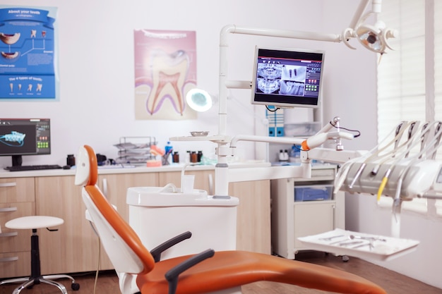 Interior do moderno gabinete de dentista e cadeira médica. armário de estomatologia sem ninguém e equipamento laranja para tratamento oral.