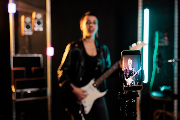 Intérprete guitarrista segurando guitarra elétrica tocando música heavy metal enquanto grava performance com telefone durante sessão de música em estúdio de áudio. músico trabalhando no novo álbum grunge antes da turnê