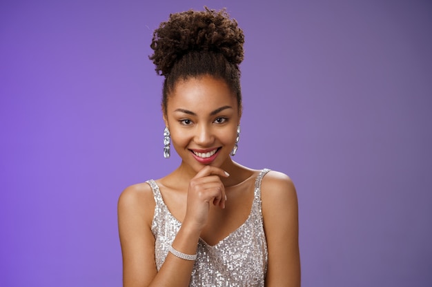 Foto grátis intrigado criativo jovem afro-americano desonesto de 20 anos garota afro penteado em prata vestido luxuoso festas tocando o queixo sorrindo misterioso tem excelente ideia inspirada planejamento, fundo azul.