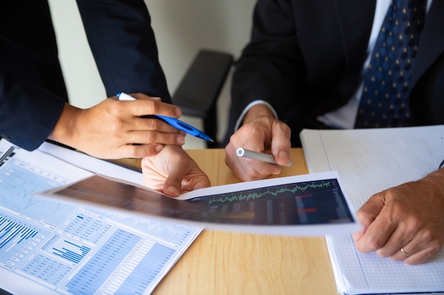 Investidor e corretor discutindo estratégia de negociação, segurando papéis com quadros financeiros e canetas. foto recortada. trabalho de corretor ou conceito de investimento