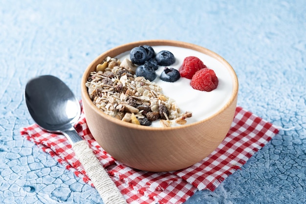 Iogurte com frutas e muesli no café da manhã na tigela sobre fundo azul