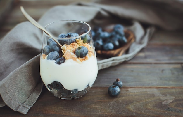 Iogurte com granola e mirtilos frescos em tigela de vidro sobre fundo de madeira velho Efeito Vintage