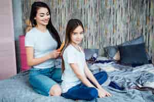 Foto grátis irmã mais velha preparando o filho para a escola e penteando o cabelo no quarto com uma escova de cabelo