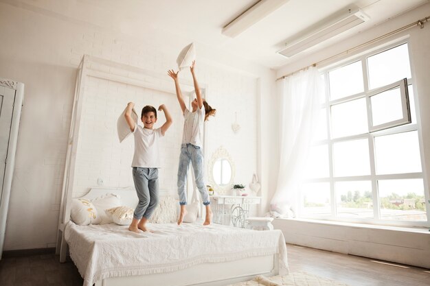 Irmão e irmã se divertindo enquanto pulando na cama no quarto