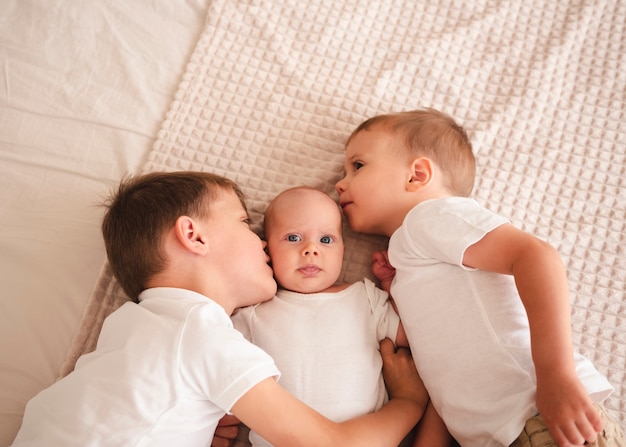 Irmãos beijando bebê recém-nascido vista superior