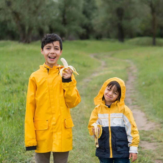 Foto grátis irmãos em capa de chuva comendo bananas