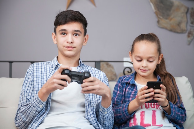 Irmãos sorridentes com smartphone e controlador