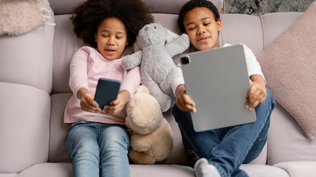 Irmãos usando tablet e celular em casa