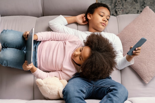 Irmãos usando tablet e celular em casa