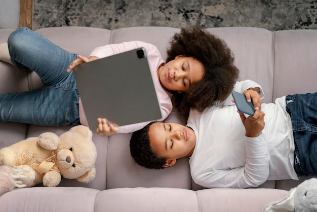 Foto grátis irmãos usando tablet e celular em casa