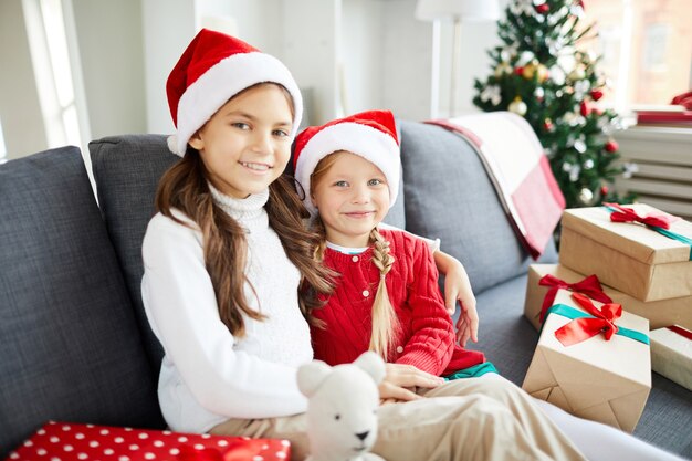 Irmãs felizes sentadas no sofá com presentes de Natal