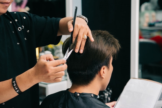 Irreconhecível cabeleireiro masculino, dando o corte de cabelo do cliente no salão