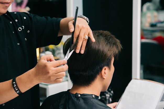 Irreconhecível cabeleireiro masculino, dando o corte de cabelo do cliente no salão