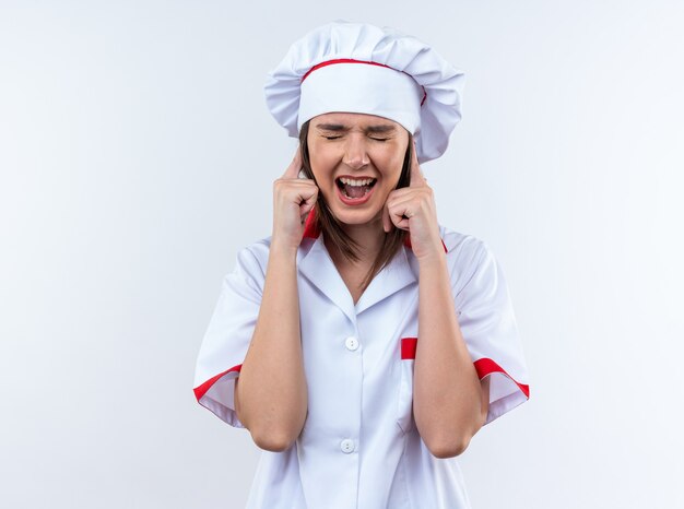 Irritada com os olhos fechados, jovem cozinheira vestindo uniforme de chef coberta com orelhas isoladas no fundo branco