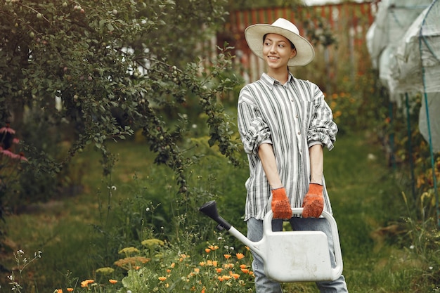 Jardinagem no verão. Mulher regando flores com um regador. Menina com um chapéu.