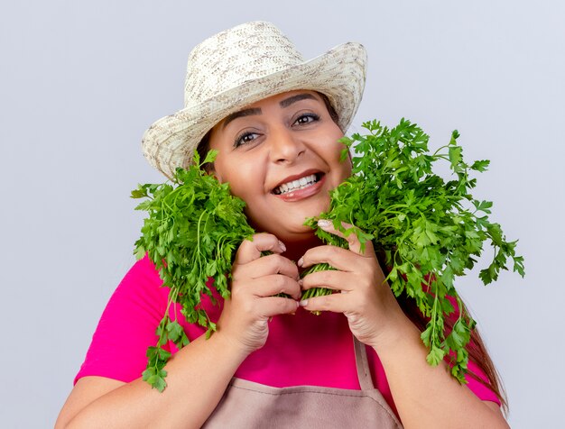Jardineira de meia-idade com avental e chapéu segurando ervas frescas