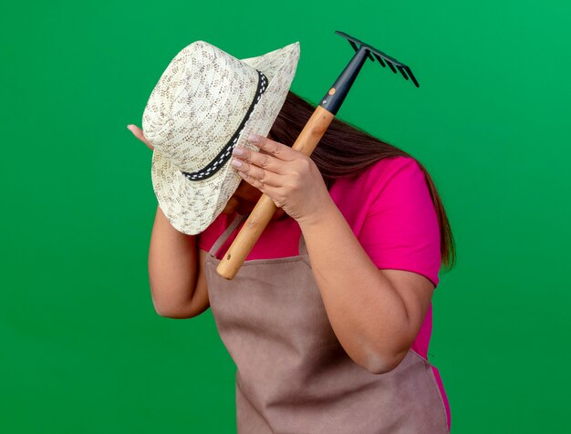 Jardineira de meia-idade com avental e chapéu segurando um mini ancinho