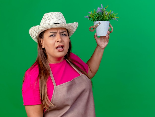 Jardineira de meia-idade com avental e chapéu segurando um vaso de plantas