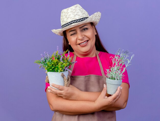 Jardineira de meia-idade com avental e chapéu segurando vasos de plantas