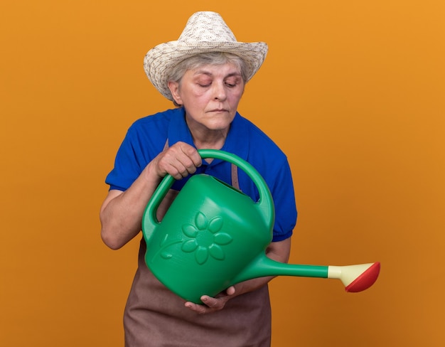 Jardineira idosa confiante usando chapéu de jardinagem segurando e olhando para o regador