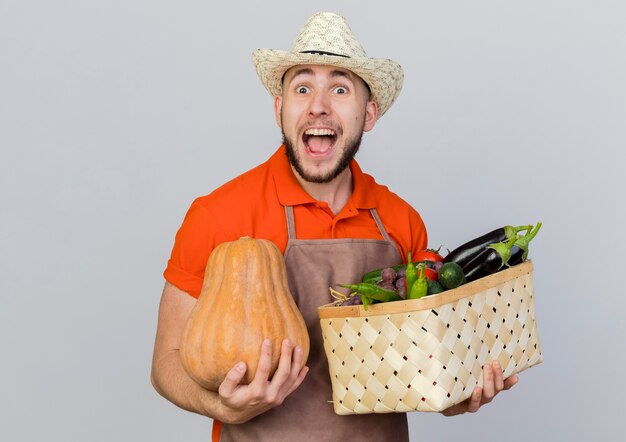 Jardineiro animado usando chapéu de jardinagem segurando uma cesta de abóbora e vegetais