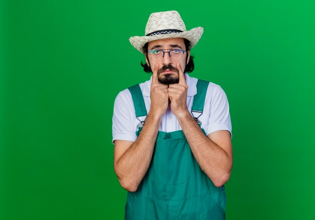 Jardineiro barbudo, homem de macacão e chapéu, com expressão triste e vai chorar