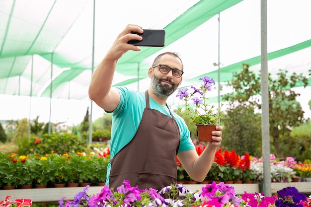 Jardineiro barbudo tirando selfie com petúnia em vaso