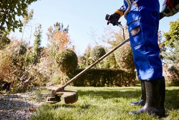 Jardineiro com weedwacker cortando a grama no jardim