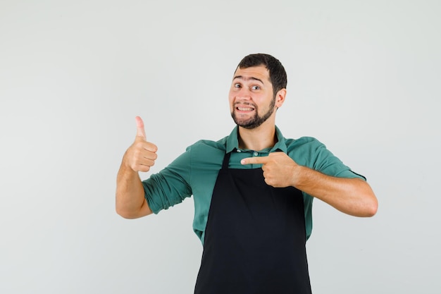 Jardineiro masculino apontando para o polegar para cima em t-shirt, avental e parecendo feliz. vista frontal.