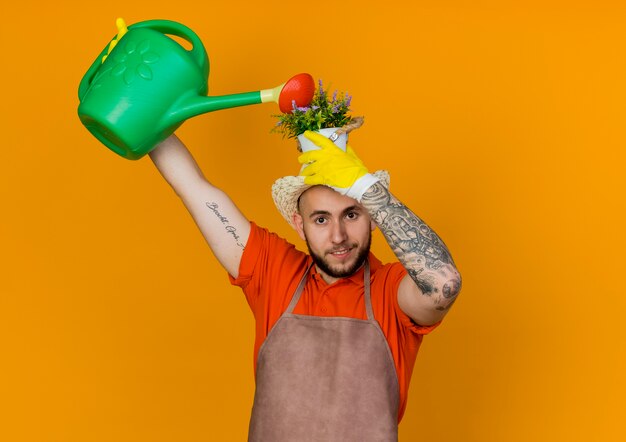 Jardineiro sorridente com chapéu de jardinagem segurando um vaso de flores na cabeça fingindo regar com um regador