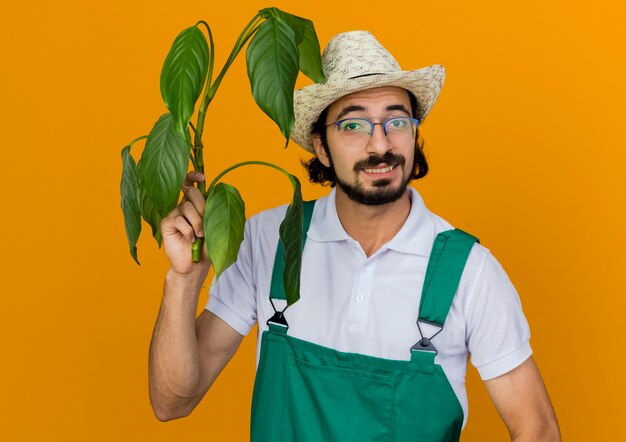 Jardineiro sorridente com óculos óticos e chapéu de jardinagem segurando a planta