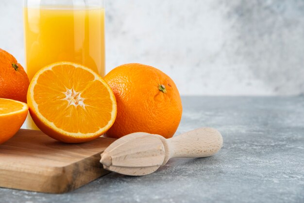 Jarra de vidro de suco com frutas fatiadas de laranja em uma placa de madeira.