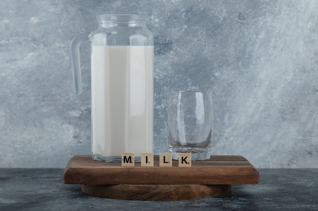 Foto grátis jarro de leite e copo de água na placa de madeira.
