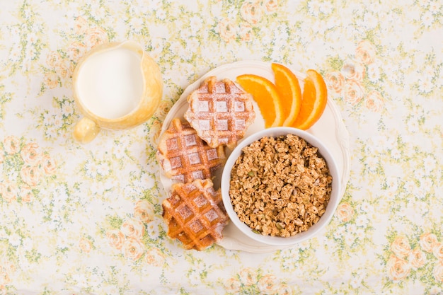 Jarro de leite e prato de tigela de granola saudável com waffles e fatia de um laranjas