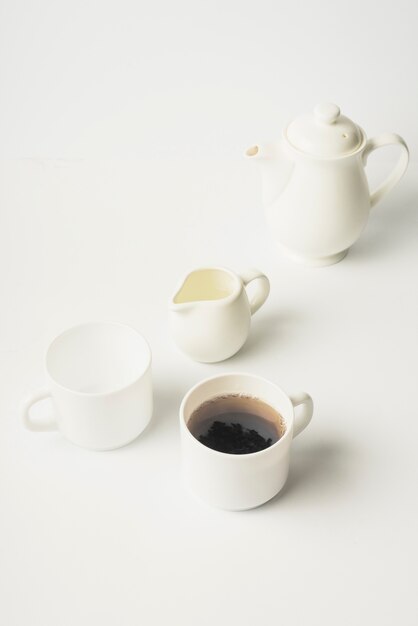 Jarro de leite; xícara de chá; copo e bule cerâmicos no fundo branco