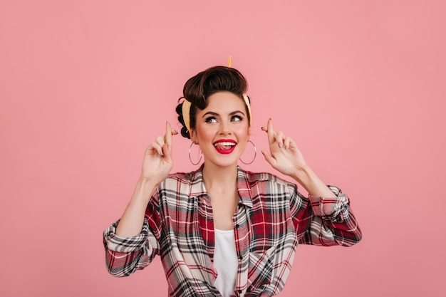 Jocund menina europeia em camisa quadriculada, posando em fundo rosa. Mulher bonita Pin-up expressando emoções positivas.