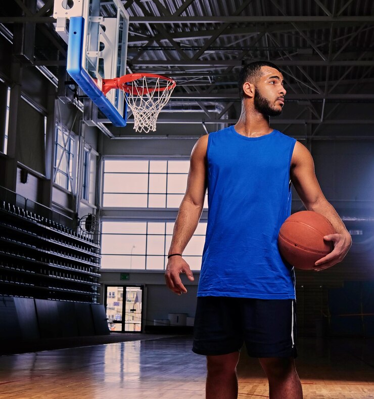 Foto grátis jogador de basquete profissional negro segura uma bola sobre o aro em um salão de jogos.