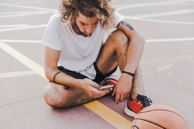 Jogador de basquete sentado no tribunal usando telefone celular