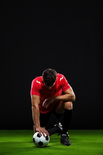 Jogador de futebol com bola de pé sobre um joelho sobre backgrou preto