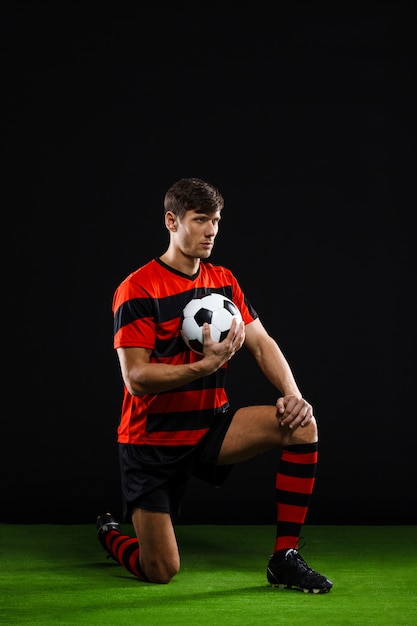 Foto grátis jogador de futebol com bola em pé no joelho, jogar futebol