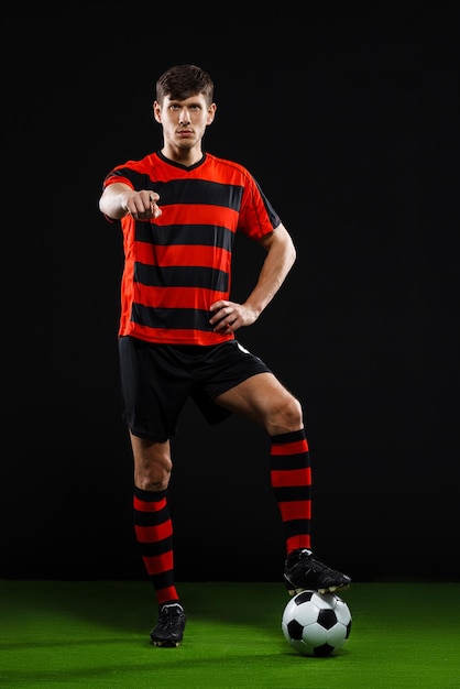 Jogador de futebol com bola em pé sobre fundo preto